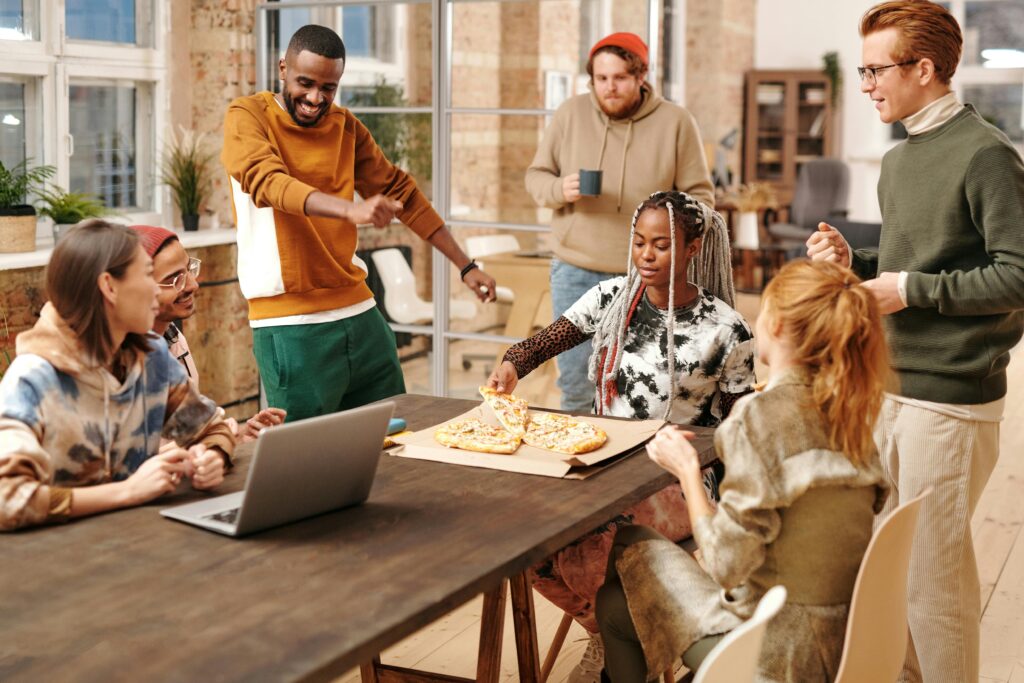 Multiracial friends enjoying pizza and laughter in a cozy indoor setting.