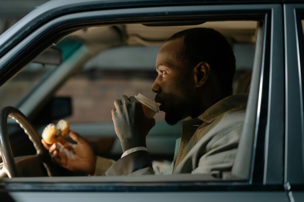 The Road Warrior's Plate - Part 1 A man sits in a car, sipping coffee and holding a donut, creating a relaxed moment.